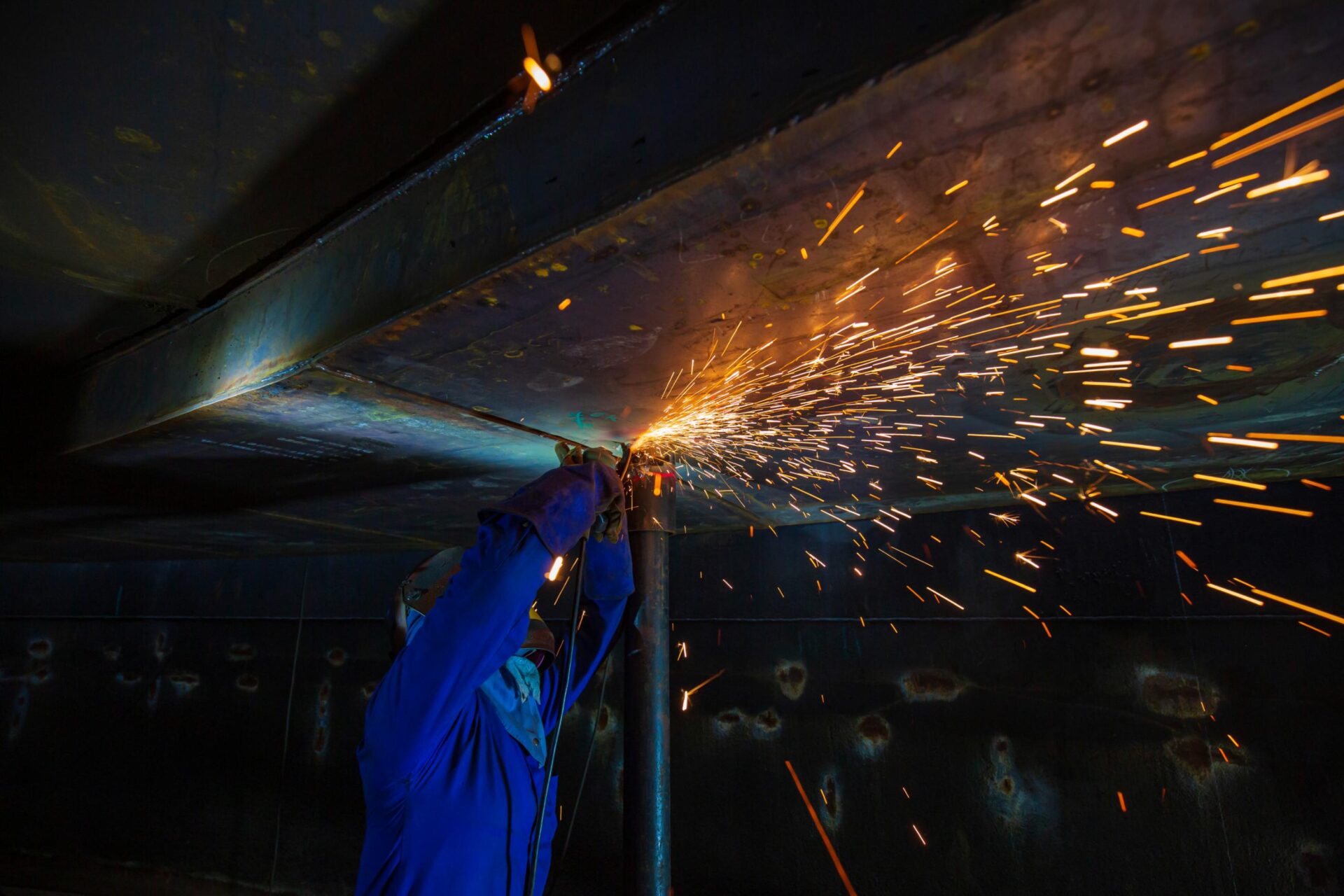 Male worker grinding steel plate with flash sparks close up wear protective gloves oil inside confined spaces